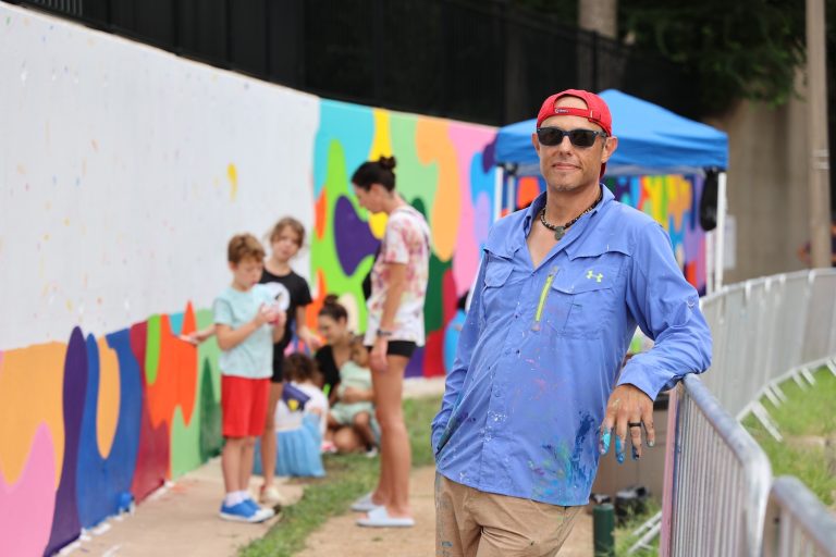 Portrait of St. Louis artist Ben Hanvy standing in front of a colorful mural.
